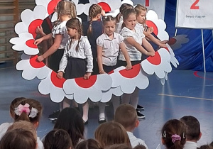Dziewczynki z klasy pierwszej podzas tańca z białoczerwonymi kwiatkami w dłoniach.