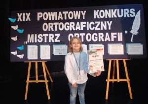 Mieszko z dyplomem na tle dekoracji.
