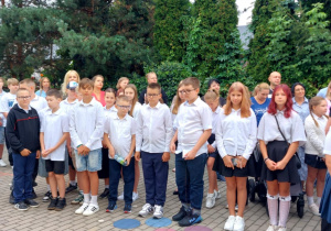 Duża grupa uczniów klasy piątej w galowych strojach poczas apelu 1 września.