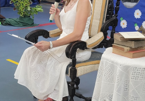 Pani Ewa Dębińska siedzi w fotelu i czyta fraszki.