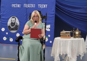 Pani Sylwia Kuniecka siedzi na foteli i czyta poezję Jana Kochanowskiego.