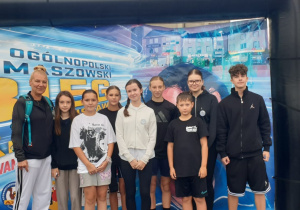 Spora grupa uczniów wraz z opiekunem na tle plakatu podczas 44 Biegu im Bronisława Malinowskiego.