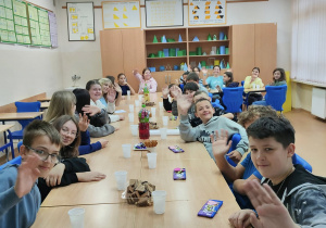 Duża grupa uczniów siedzi za stołem podczas poczęstunku z okazji Dnia Chłopaka.