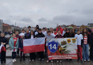 Duża grupa uczniów wraz nauczycielem wychowania fizycznego z szkolnym banaerem tuz przed Biegiem Niepodległości.
