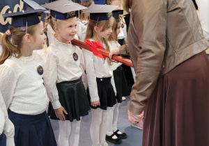 Pani dyrektor Ewa Brzezińska symbolicznym dużym ołowkiem pasuje uczniów klasy pierwszej.