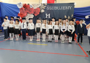 Duża grupa uczniów klasy pierwszej ślubuje podczas aktu pasowania.