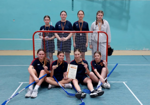 Reprezentacja szkoły w unihokeju na tle bramki.