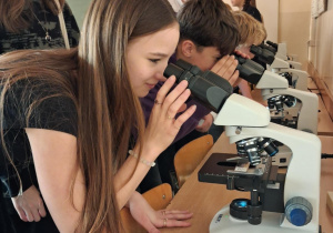 Uczennica patrzy przez mikroskop.