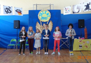 Grupa uczniów nagrodzona statuetkami "Mam talent" na niebieskim tle dekoracji.