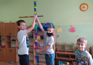 Chłopcy prezentują najwyższą wieżę z kolorowych kloców. Dwóch stoi na krzesełkach i trzyma wieżę aby się nie przewróciła